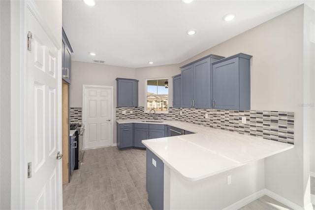 kitchen featuring a breakfast bar, backsplash, sink, stainless steel gas range, and kitchen peninsula