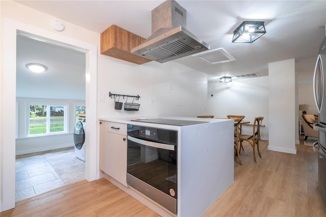 kitchen with stainless steel oven, light hardwood / wood-style flooring, washer / dryer, island range hood, and black electric stovetop