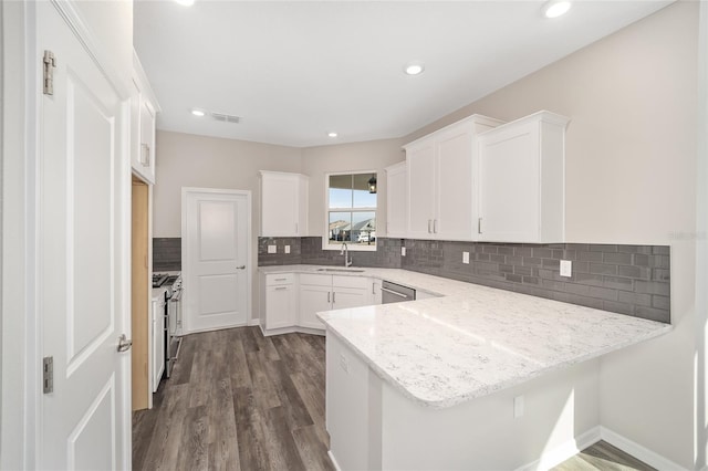 kitchen with light stone countertops, kitchen peninsula, white cabinetry, and sink