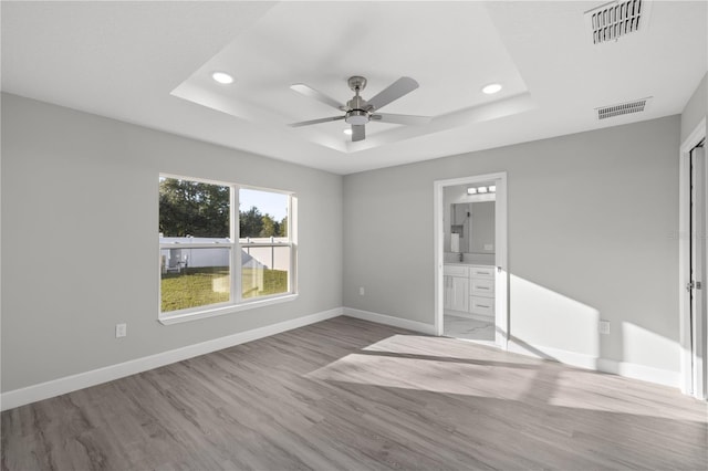 unfurnished bedroom featuring ceiling fan, a raised ceiling, light wood-type flooring, and ensuite bathroom