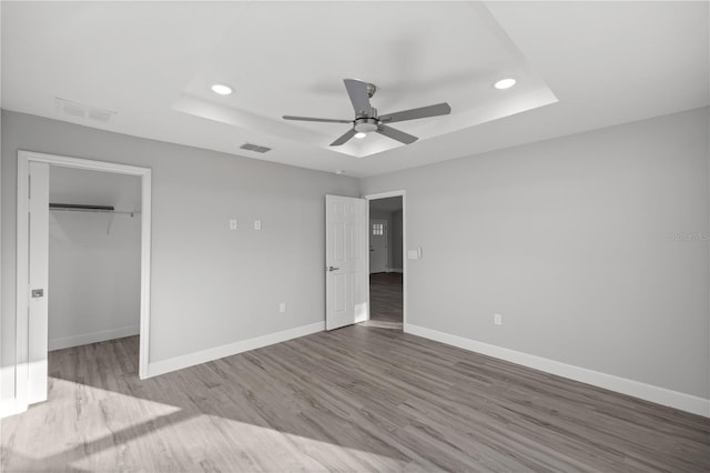 unfurnished bedroom with a spacious closet, ceiling fan, light hardwood / wood-style floors, a tray ceiling, and a closet