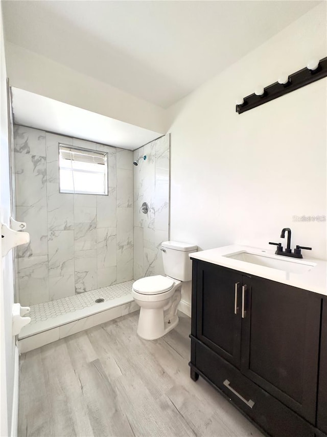 bathroom featuring vanity, toilet, wood-type flooring, and a tile shower