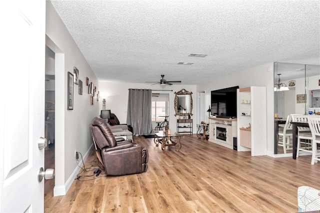 living room with ceiling fan with notable chandelier, a textured ceiling, and light hardwood / wood-style flooring