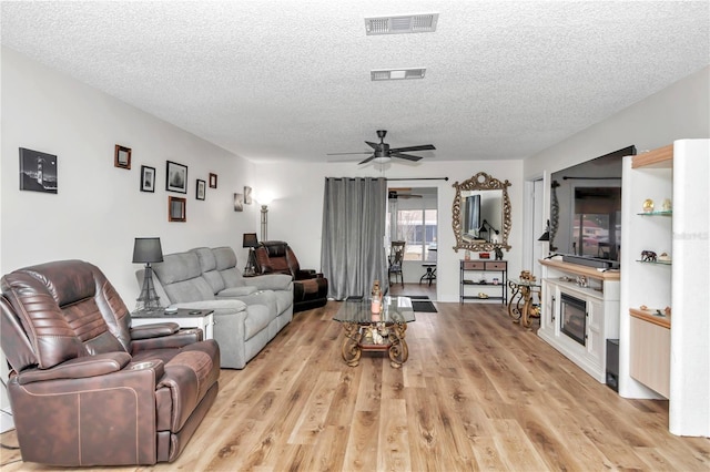 living room with a textured ceiling, ceiling fan, and light hardwood / wood-style flooring