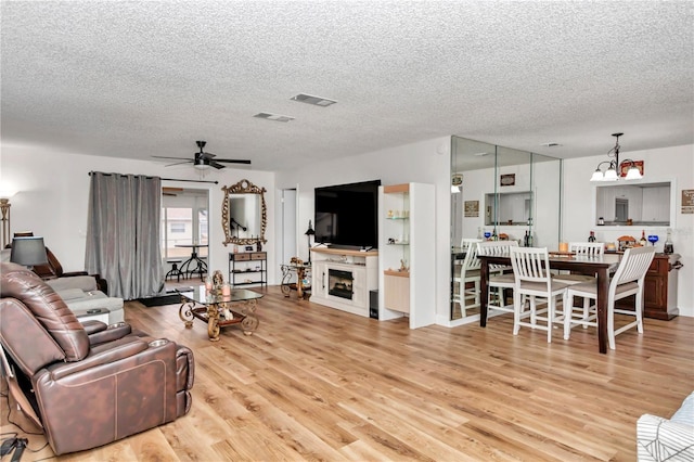 living room with a textured ceiling, ceiling fan with notable chandelier, and light wood-type flooring