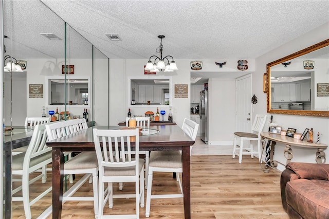 dining area with a notable chandelier, a textured ceiling, and light hardwood / wood-style floors