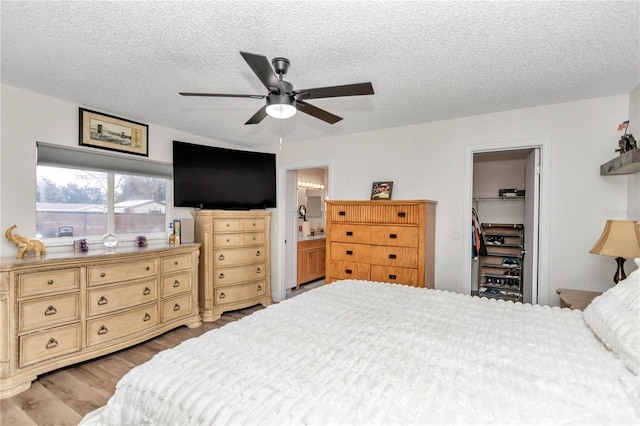 bedroom with a textured ceiling, a walk in closet, connected bathroom, a closet, and ceiling fan