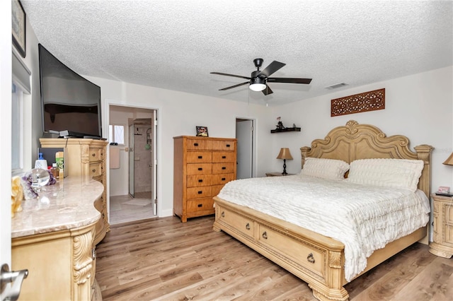 bedroom with ceiling fan, a textured ceiling, ensuite bathroom, and light wood-type flooring