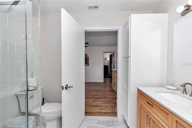 bathroom with toilet, vanity, walk in shower, and a textured ceiling