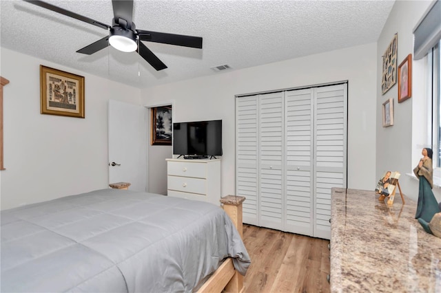 bedroom with a textured ceiling, ceiling fan, a closet, and light wood-type flooring