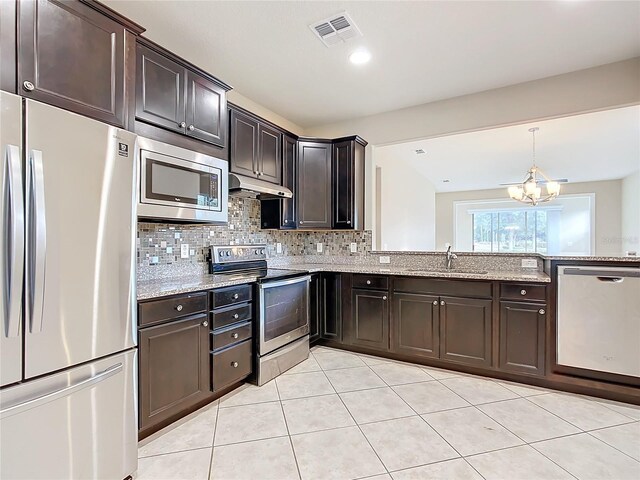 kitchen with appliances with stainless steel finishes, light stone counters, dark brown cabinets, sink, and an inviting chandelier