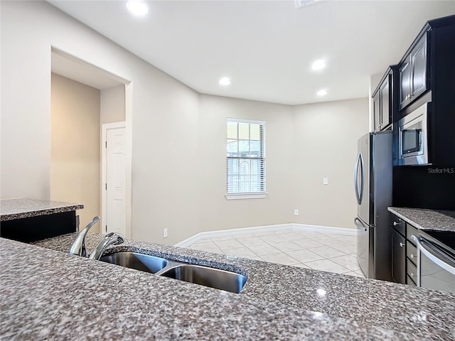 kitchen featuring appliances with stainless steel finishes, light tile patterned floors, dark stone countertops, and sink