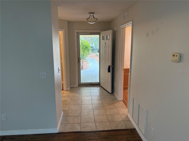 doorway featuring light tile patterned floors, a textured ceiling, visible vents, and baseboards