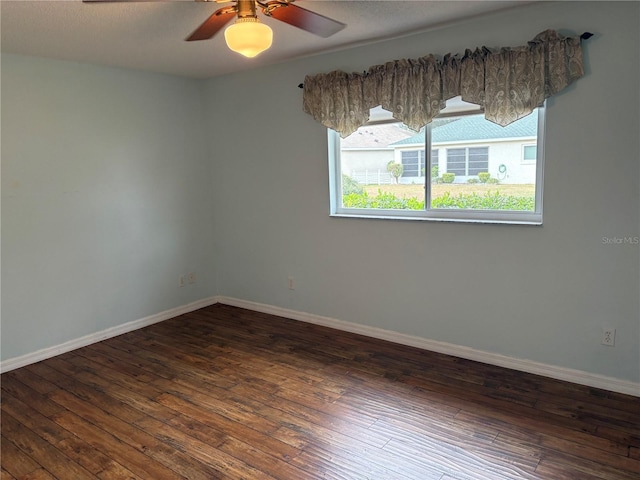 spare room featuring dark wood-style floors, ceiling fan, and baseboards