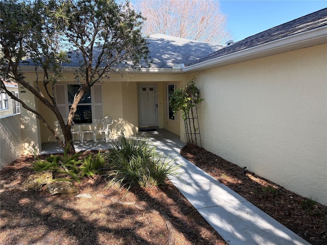 property entrance with roof with shingles and stucco siding