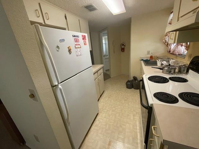 kitchen featuring white cabinets, white appliances, a textured ceiling, and range hood