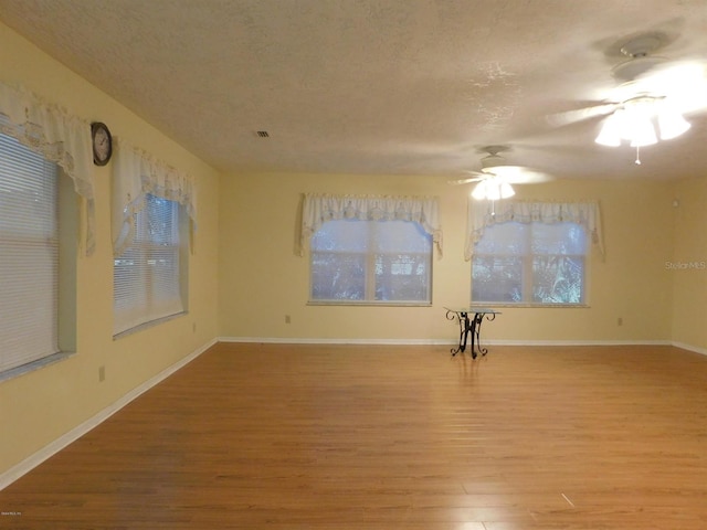 empty room with ceiling fan, light wood-type flooring, and a textured ceiling