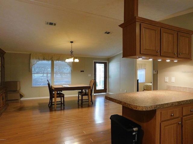 kitchen with decorative light fixtures, light wood-type flooring, ornamental molding, and an inviting chandelier