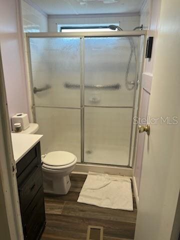 bathroom featuring wood-type flooring, vanity, toilet, and a shower with door