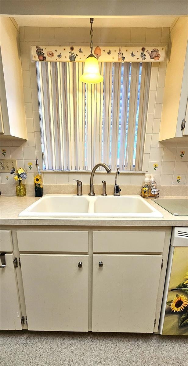 kitchen featuring pendant lighting, white cabinetry, sink, and tasteful backsplash