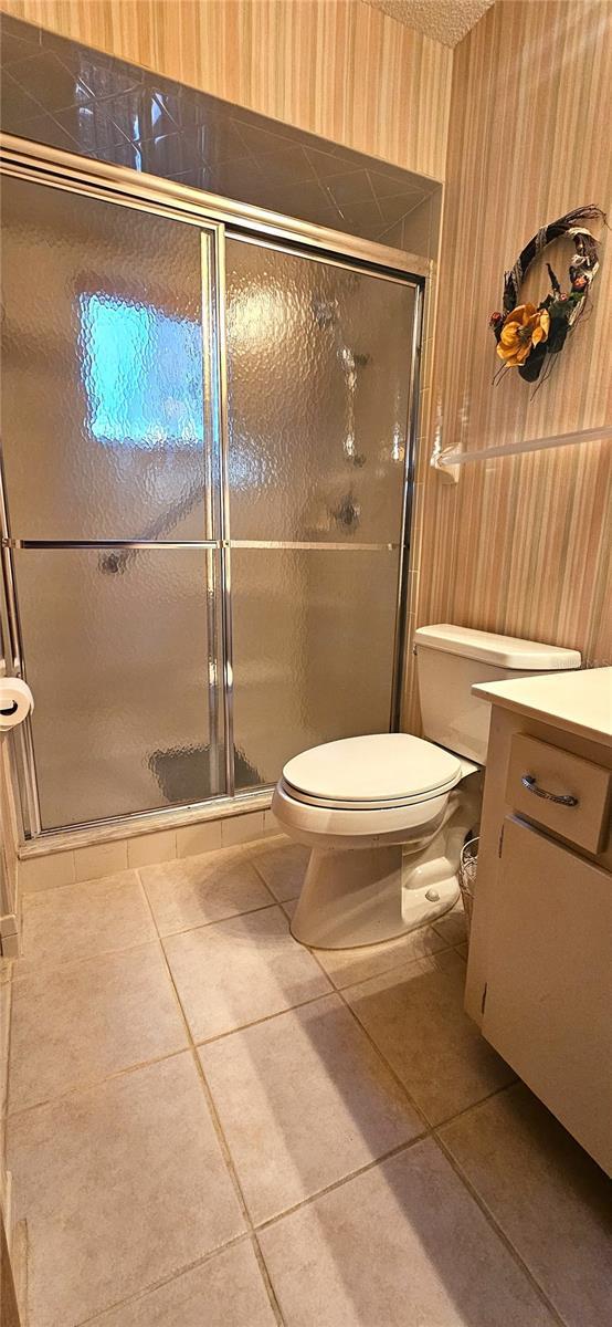 bathroom featuring tile patterned flooring, vanity, toilet, and a shower with door