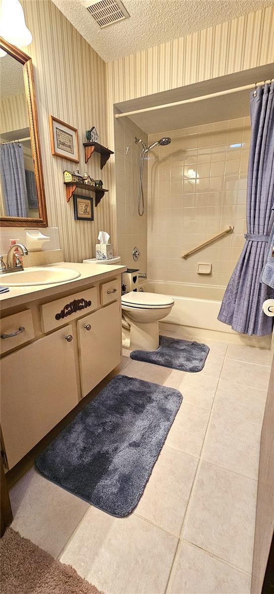 full bathroom featuring shower / bath combination with curtain, tile patterned floors, vanity, a textured ceiling, and toilet