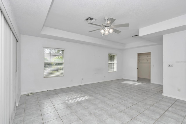 tiled spare room with a tray ceiling, ceiling fan, and a textured ceiling