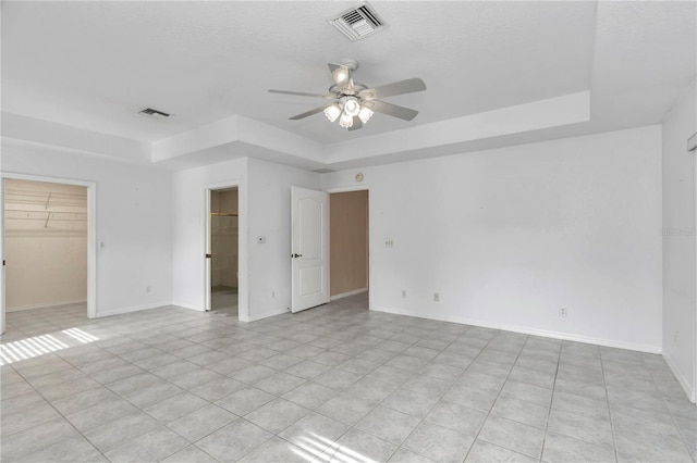 unfurnished bedroom featuring ceiling fan, a raised ceiling, a walk in closet, and a closet