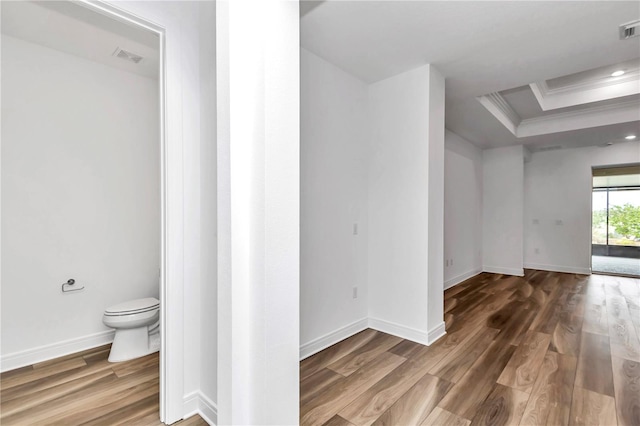 interior space with a tray ceiling, toilet, ornamental molding, and hardwood / wood-style flooring