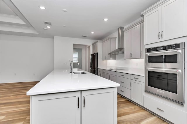 kitchen with double oven, sink, wall chimney range hood, a center island with sink, and fridge