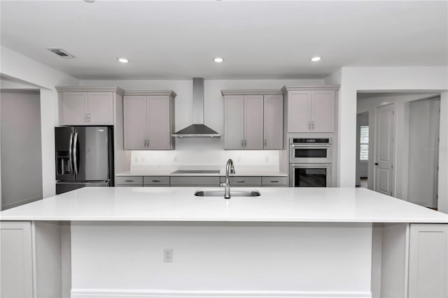 kitchen featuring appliances with stainless steel finishes, gray cabinetry, wall chimney exhaust hood, sink, and a large island