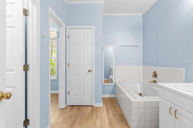 bathroom with vanity, hardwood / wood-style flooring, a relaxing tiled tub, and crown molding