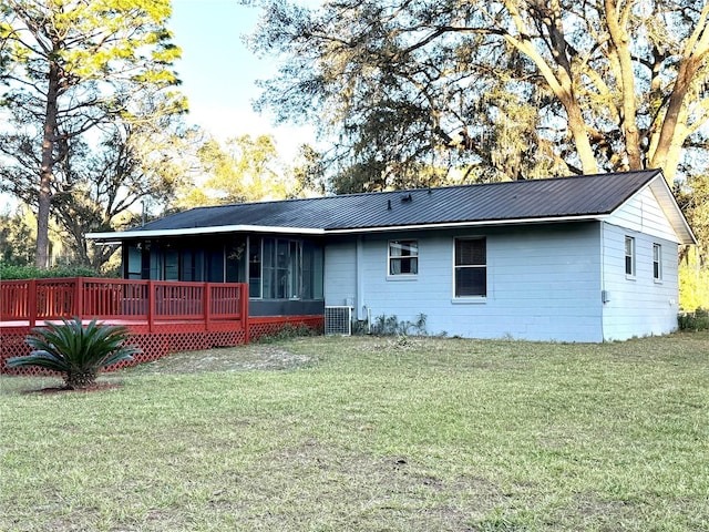 rear view of property with a sunroom, central AC unit, a wooden deck, and a lawn