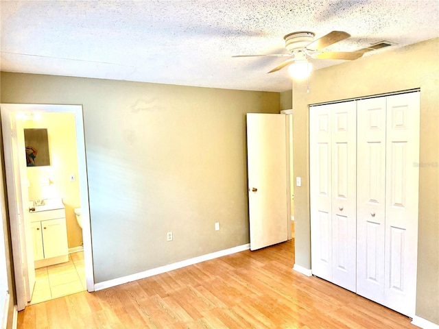 unfurnished bedroom with ceiling fan, light hardwood / wood-style flooring, ensuite bathroom, a textured ceiling, and a closet