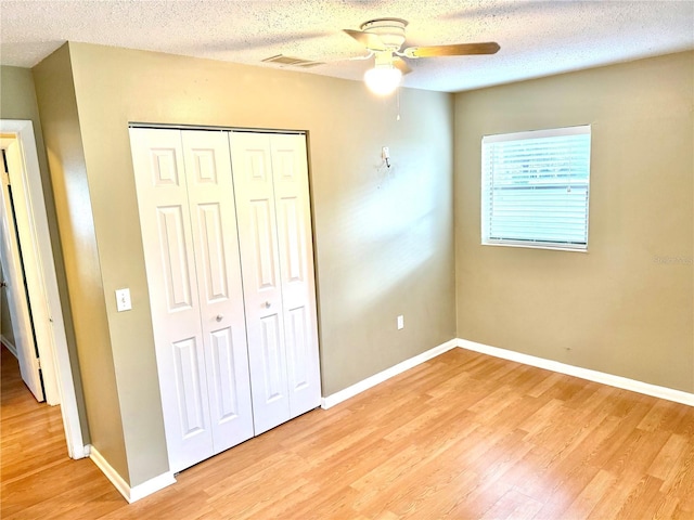 unfurnished bedroom with a textured ceiling, light hardwood / wood-style flooring, a closet, and ceiling fan