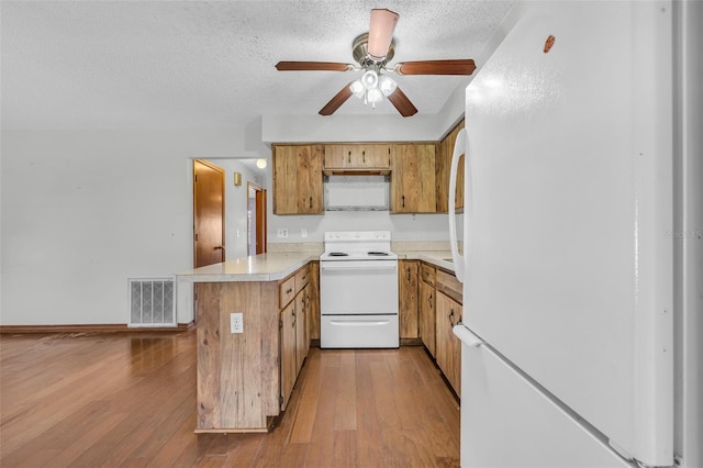 kitchen featuring kitchen peninsula, a textured ceiling, white appliances, and light hardwood / wood-style floors