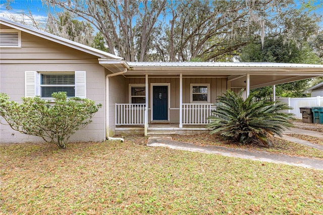 doorway to property featuring a porch, a carport, and a lawn