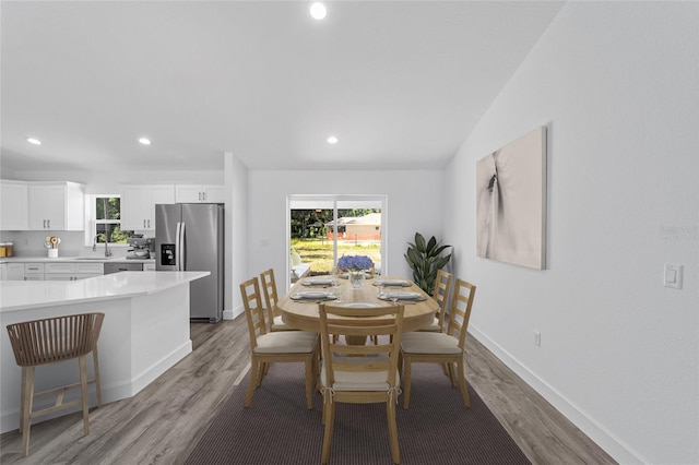 dining area featuring light hardwood / wood-style floors, vaulted ceiling, and sink