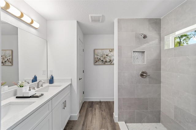 bathroom with hardwood / wood-style flooring, vanity, a textured ceiling, and tiled shower