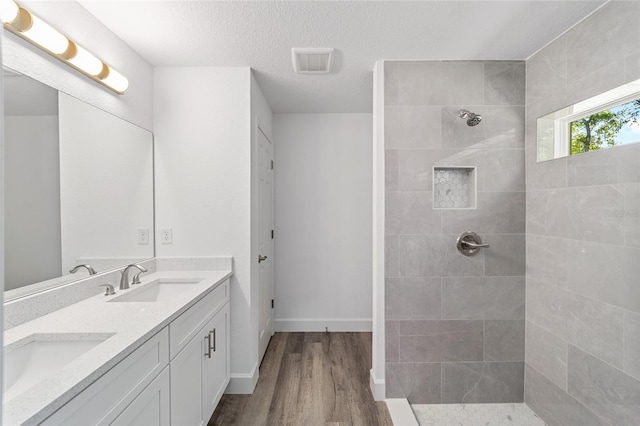 bathroom with vanity, wood-type flooring, a textured ceiling, and tiled shower