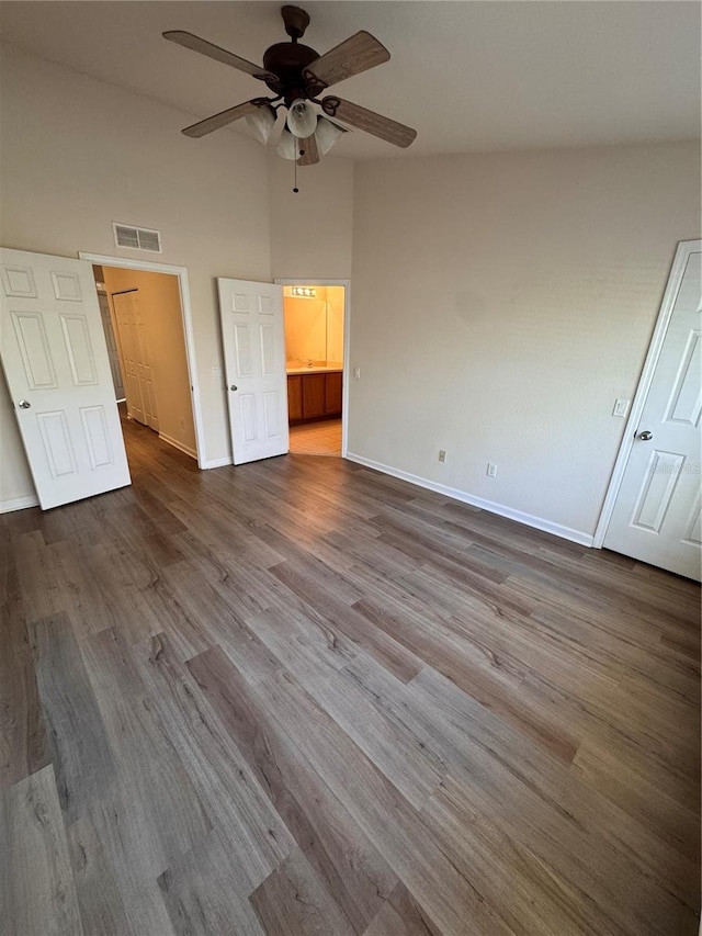 unfurnished bedroom with ceiling fan, ensuite bath, wood-type flooring, and a high ceiling