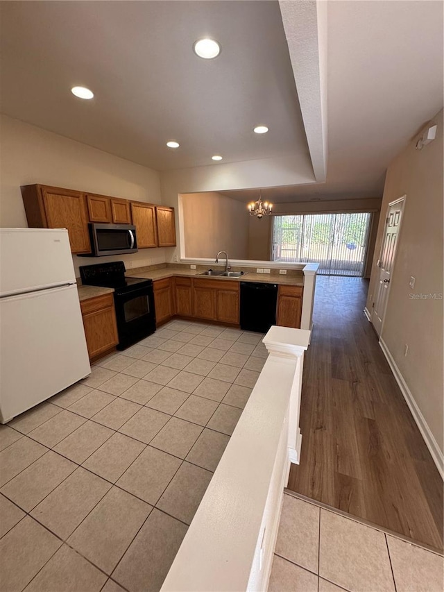 kitchen with light tile patterned floors, kitchen peninsula, a notable chandelier, decorative light fixtures, and black appliances