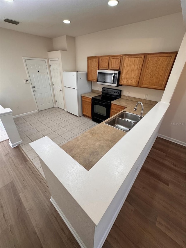 kitchen with white fridge, black range with electric cooktop, sink, kitchen peninsula, and light tile patterned floors