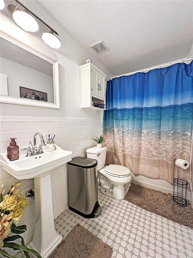 bathroom with shower / bath combination with curtain, toilet, a textured ceiling, and tile walls