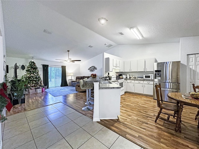 kitchen featuring lofted ceiling, white appliances, kitchen peninsula, light tile patterned flooring, and white cabinetry