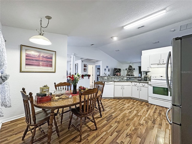 dining area with a textured ceiling, vaulted ceiling, and light hardwood / wood-style flooring