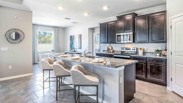 kitchen featuring a kitchen bar, dark brown cabinetry, stainless steel appliances, and an island with sink