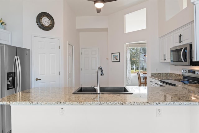 kitchen with white cabinetry, sink, ceiling fan, stainless steel appliances, and light stone counters