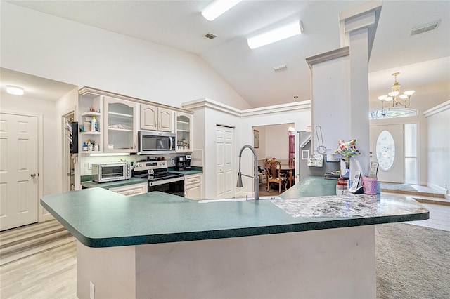 kitchen featuring kitchen peninsula, appliances with stainless steel finishes, sink, an inviting chandelier, and lofted ceiling