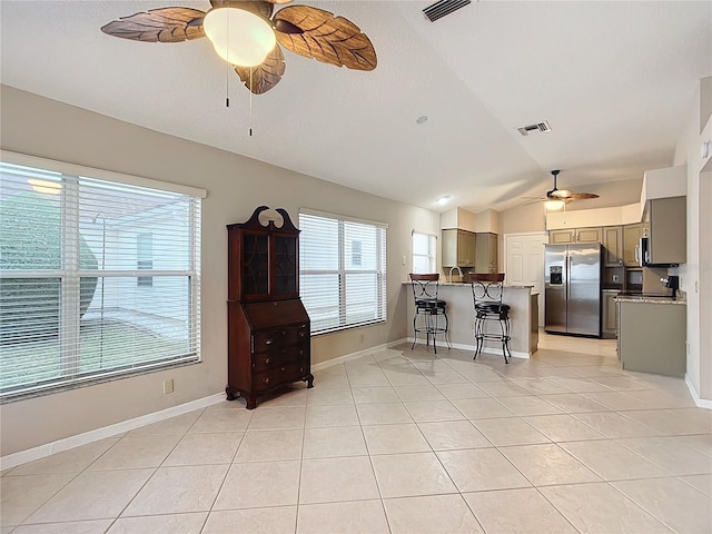 kitchen with a kitchen breakfast bar, stainless steel fridge with ice dispenser, light tile patterned flooring, and lofted ceiling